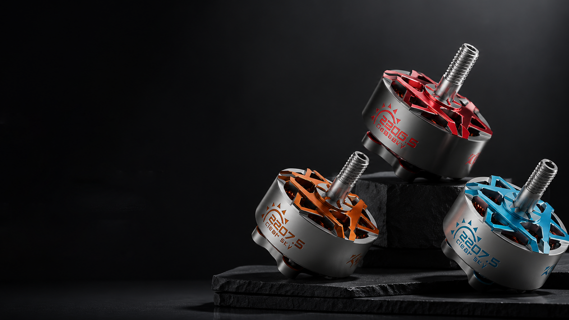 Three brushed metal brushless motor hubs with silver splined shafts, arranged on a black stone riser against a dark studio background. The hubs feature red, orange, and blue anodized outer rings with visible 'zenirace' branding.