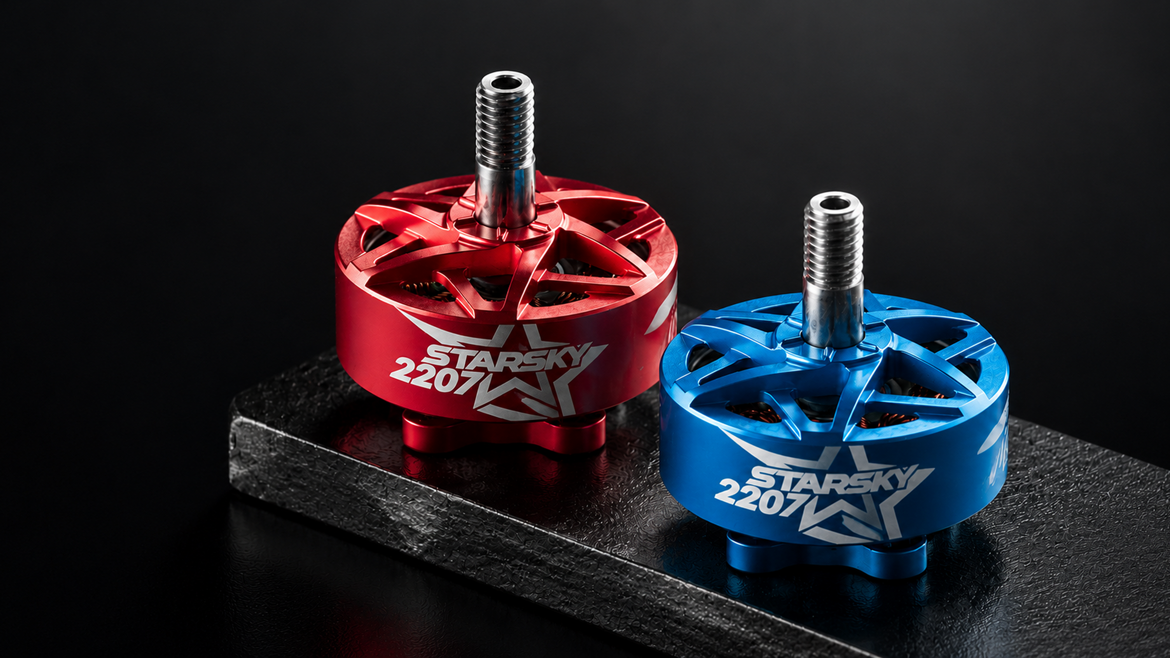 Two ZeniRace 2207 brushed motor anodized aluminum components, one in red and one in blue, displayed on a black textured surface against a dark background.