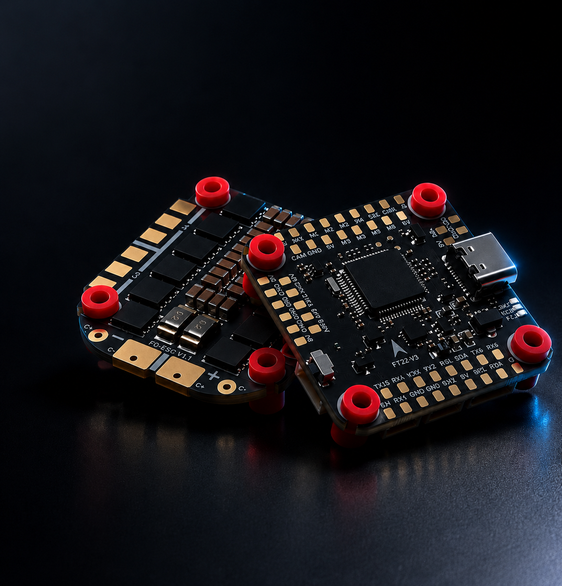 Two black electronic flight control boards with gold-plated contacts and red terminal caps, photographed on a dark reflective surface.